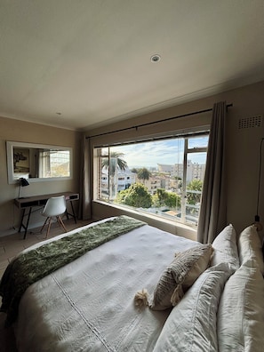Ein Schlafzimmer mit einem großen Bett, einem Schreibtisch und einem Fenster mit Blick auf die Stadt.