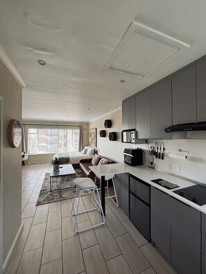 A modern kitchen with grey cabinets, a black range hood, and a dining area with a white table and chairs. - Beautiful studio apartment, with a stunning view! (Cape Town)