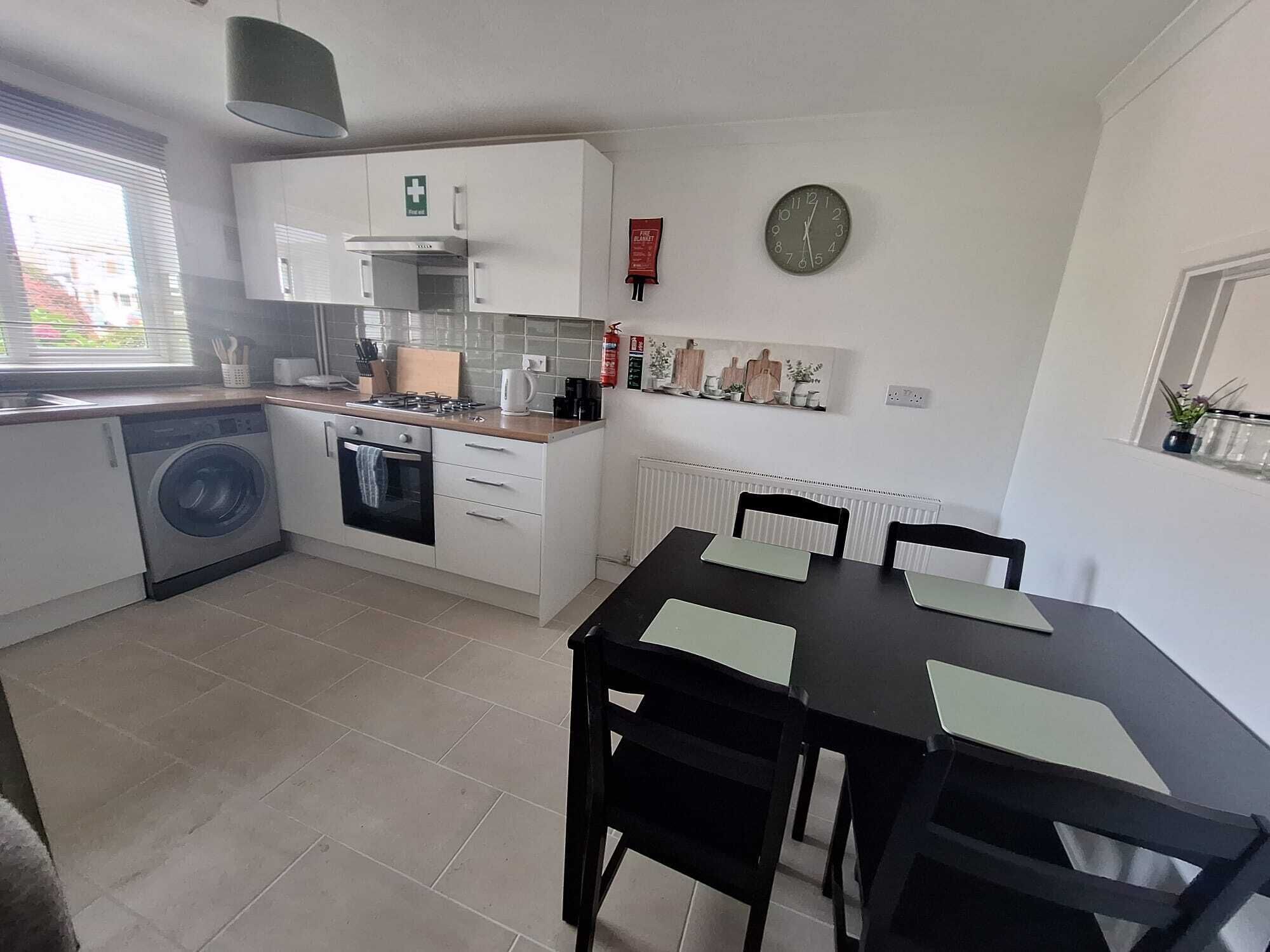 A compact kitchen with a washing machine, oven, and a dining table with chairs.