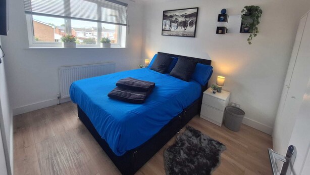 A bedroom with a bed, a window, a radiator, a bedside table, a lamp, and a wall-mounted picture. - 3 BEDROOM + LIVING, Terrace House, Sleeps up to 7 people  with Garden (Cardiff)