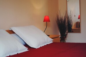A bed with white pillows, a red blanket, a red lamp, and a mirror on the wall.
