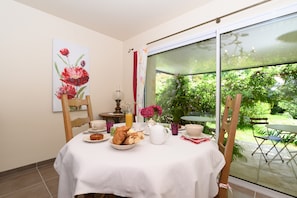 Une table à manger avec des aliments pour le petit-déjeuner, un tableau et une vue sur un jardin, visible à travers une porte vitrée.