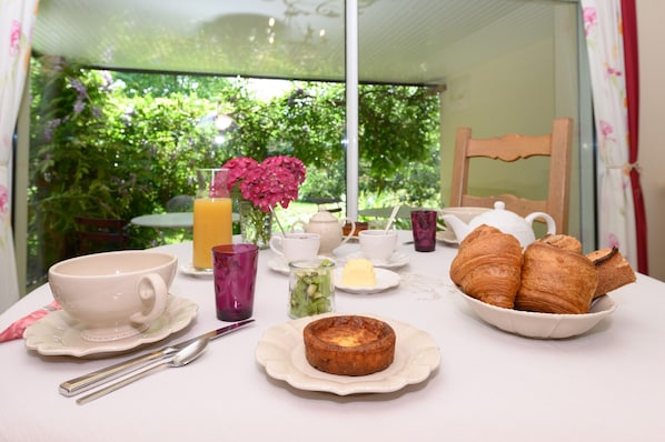 Una mesa de desayuno con una taza, tetera, croissants y una pequeña tarta.