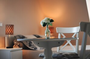 Una stanza con un tavolo in vetro, una sedia bianca, un comodino, una lampada e un letto con un cuscino decorato.