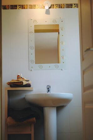 Une salle de bain avec un lavabo blanc, un miroir orné de motifs décoratifs et un porte-serviettes.