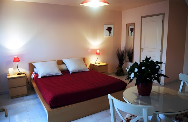 Une chambre à coucher comprenant un lit, des lampes de chevet, une table de chevet, une table ronde avec des chaises et une plante en pot.