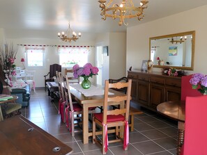 Un coin repas avec une table en bois, des chaises, un vase de fleurs, un lustre et un miroir au mur.