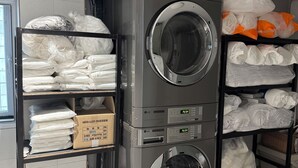 A laundry room with stacked laundry bags on shelves, a washing machine, and a dryer. - The dongdaemun hostel (Seoul)