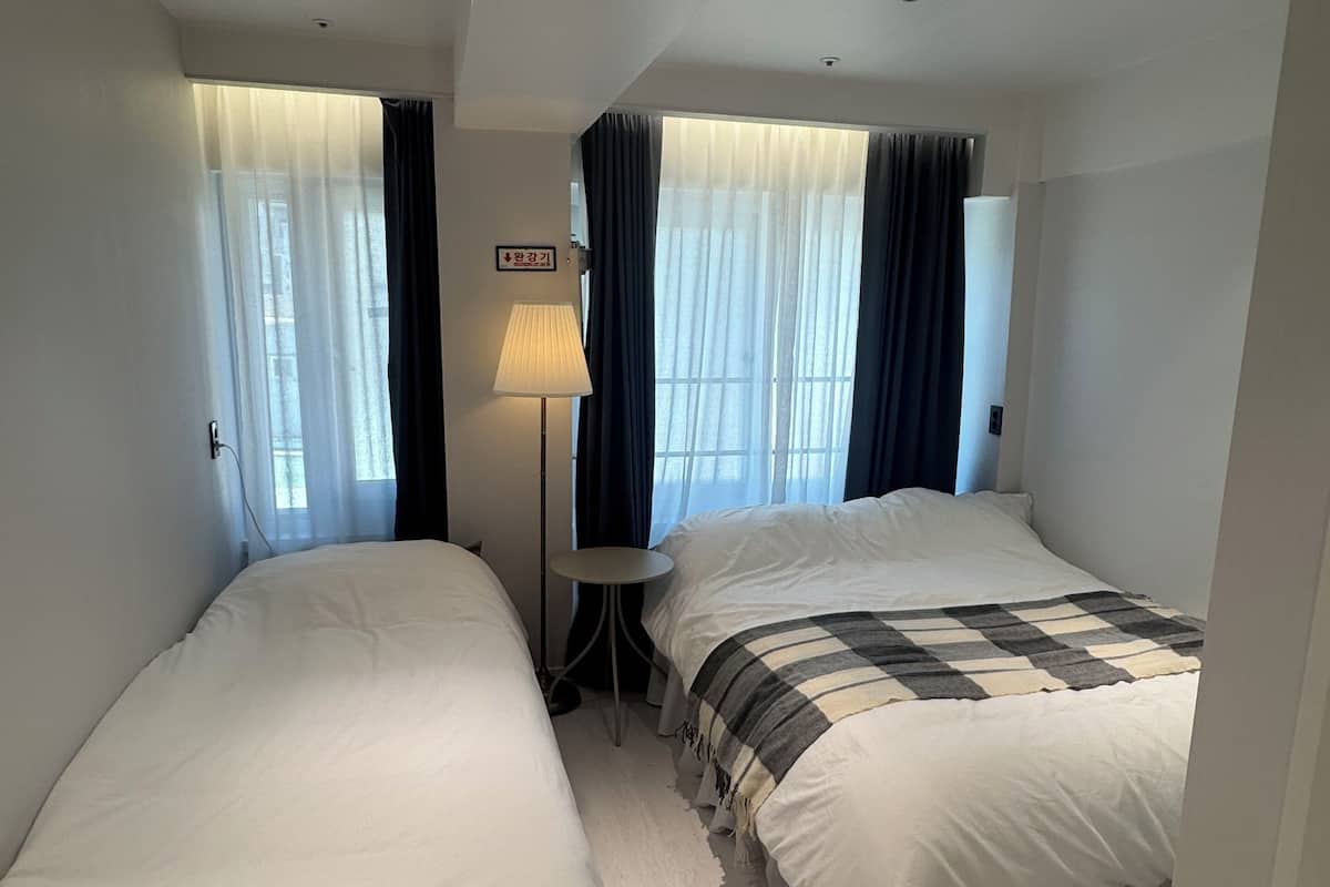 Une chambre d’hôtel avec deux lits, une petite table, une lampe et un luminaire au plafond.