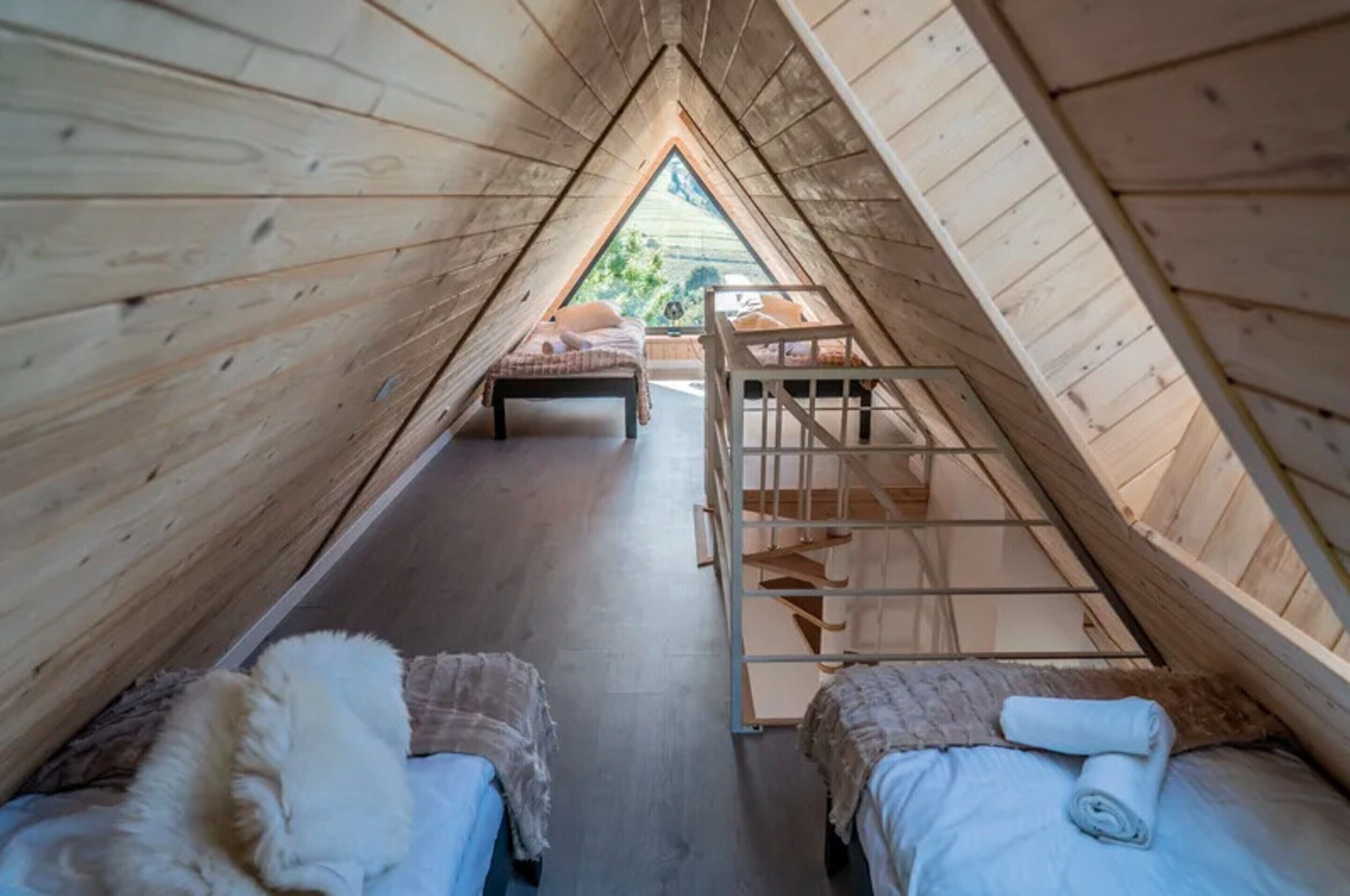 An attic room with wooden walls, a loft bed, a small staircase, and two beds with blankets.