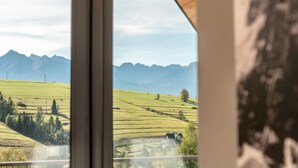 A view through a window with a mountain landscape, including a house and a cow. - Holiday Home With Sauna and Mountain View (Bukowina Tatrzanska)
