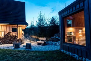 A wooden cabin with a large window, a stack of firewood, and a stone wall. - Holiday Home With Sauna and Mountain View (Bukowina Tatrzanska)