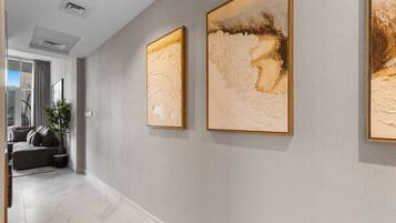 A hallway with two large abstract paintings, a grey sofa, and a potted plant.