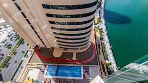 A high-rise hotel with a pool area, a curved facade, and a waterfront view. - Gogoto4 2BR Premium Canal & Burj Khalifa View (Dubai)