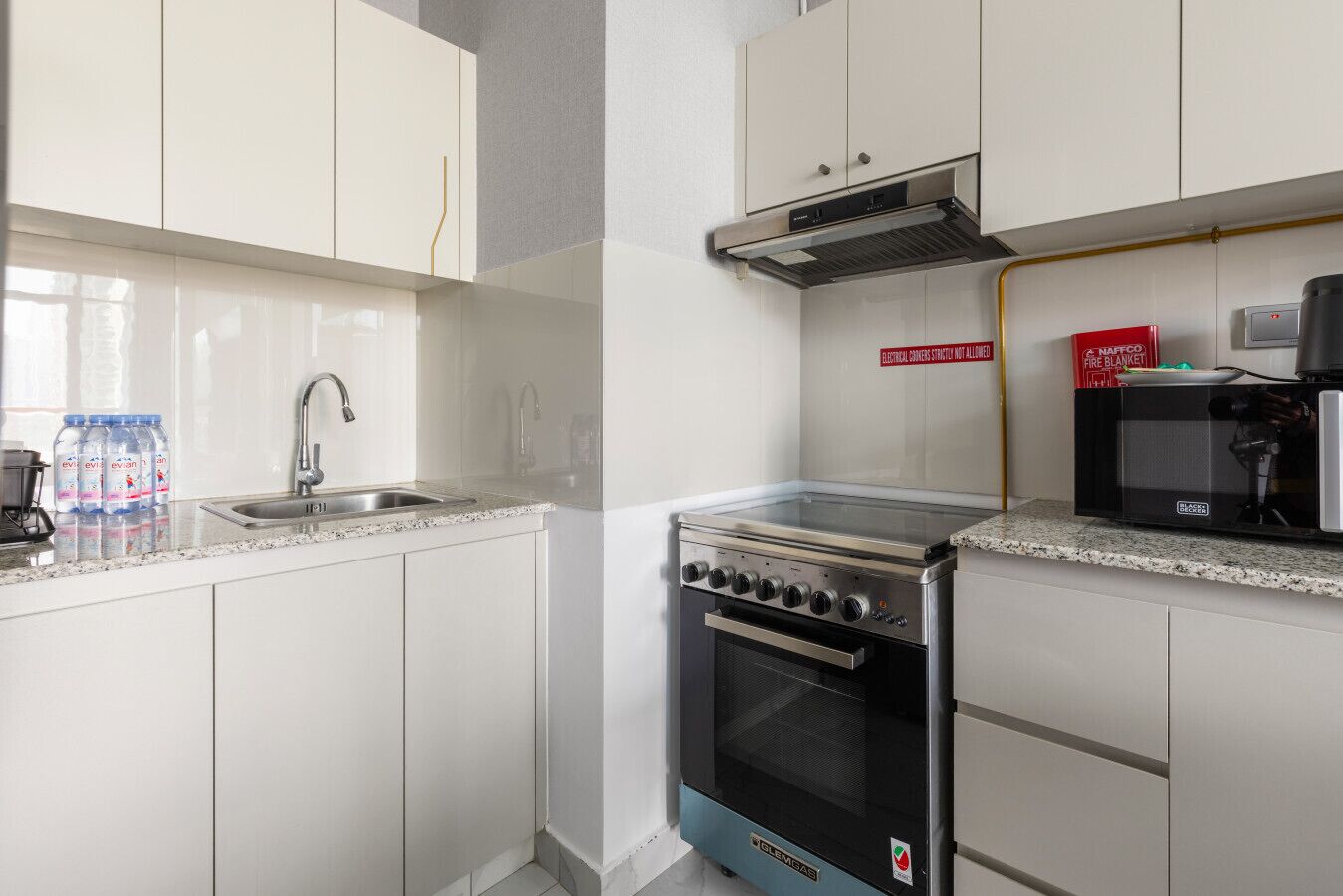 A kitchen with white cabinets, a stainless steel sink, a black stove, and a coffee machine.