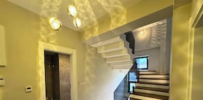 A modern staircase with a glass railing, a wall-mounted television, and a door leading to another room.