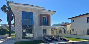 A modern house with a stone facade, large windows, a pool, and outdoor seating.