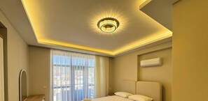 Una habitación de hotel con cama, lámpara en el techo, ventana con cortinas y un aire acondicionado en la pared.