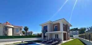 Una casa moderna de dos pisos con piscina, mobiliario exterior y un césped bien cuidado.