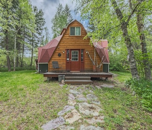 A wooden cabin with a red roof, a front door, and a porch with steps leading up to it. - Gateway to Glacier (Columbia Falls)