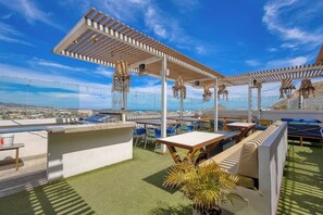 An outdoor terrace with a pergola, seating, and a view of the city. - Hotel Room With Ocean-view Rooftop Infinity Pool, AC, Gym - Dog-friendly (Cabo San Lucas)