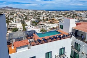 Ein Pool auf dem Dach mit Liegestühlen, Blick auf die Stadt und ein weiter Bergrücken im Hintergrund.