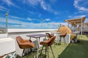 Eine Dachterrasse mit Sitzgelegenheiten im Freien, einem Grillbereich und Blick auf die Stadt.