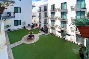 A courtyard with artificial grass, a central fountain, outdoor seating, and a white building with balconies. - Hotel Room With Ocean-view Rooftop Infinity Pool, AC, Gym - Dog-friendly (Cabo San Lucas)