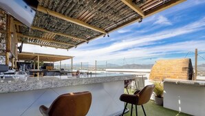 A rooftop bar with a stone wall, bar stools, and a view of the cityscape. - Hotel Room With Ocean-view Rooftop Infinity Pool, AC, Gym - Dog-friendly (Cabo San Lucas)