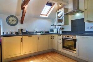 A kitchen with wooden beams, a skylight, a clock, and modern appliances. - Little Norley (Northlew)