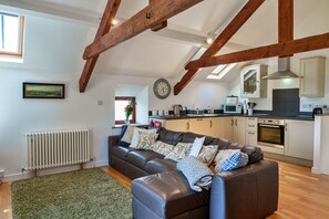 A modern kitchen with wooden beams, a dining area with a brown leather sofa, and a view of the countryside through a window. - Little Norley (Northlew)