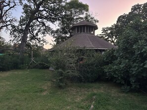 Ein Pavillon mit Ziegeldach, umgeben von dichtem Grün und einer Rasenfläche.