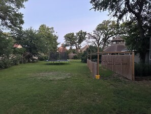 Un patio trasero con un trampolín, cerca de madera y árboles.
