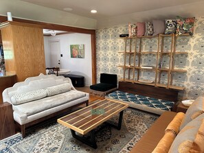 A living room with a sofa, a coffee table, a patterned rug, a bookshelf, and a painting on the wall.
