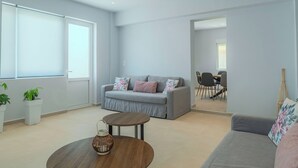 A modern living room with a grey sofa, a round coffee table, and a dining area in the background.