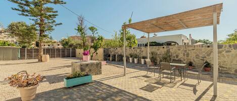 An outdoor patio area with a pergola, seating, and potted plants.