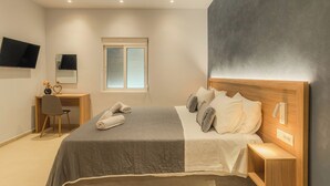 A bedroom with a bed, bedside table, nightstand, desk, chair, and a TV mounted on the wall.