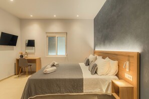 A bedroom with a bed, bedside table, nightstand, desk, chair, and a TV mounted on the wall. - Aspasia House (Platanias)
