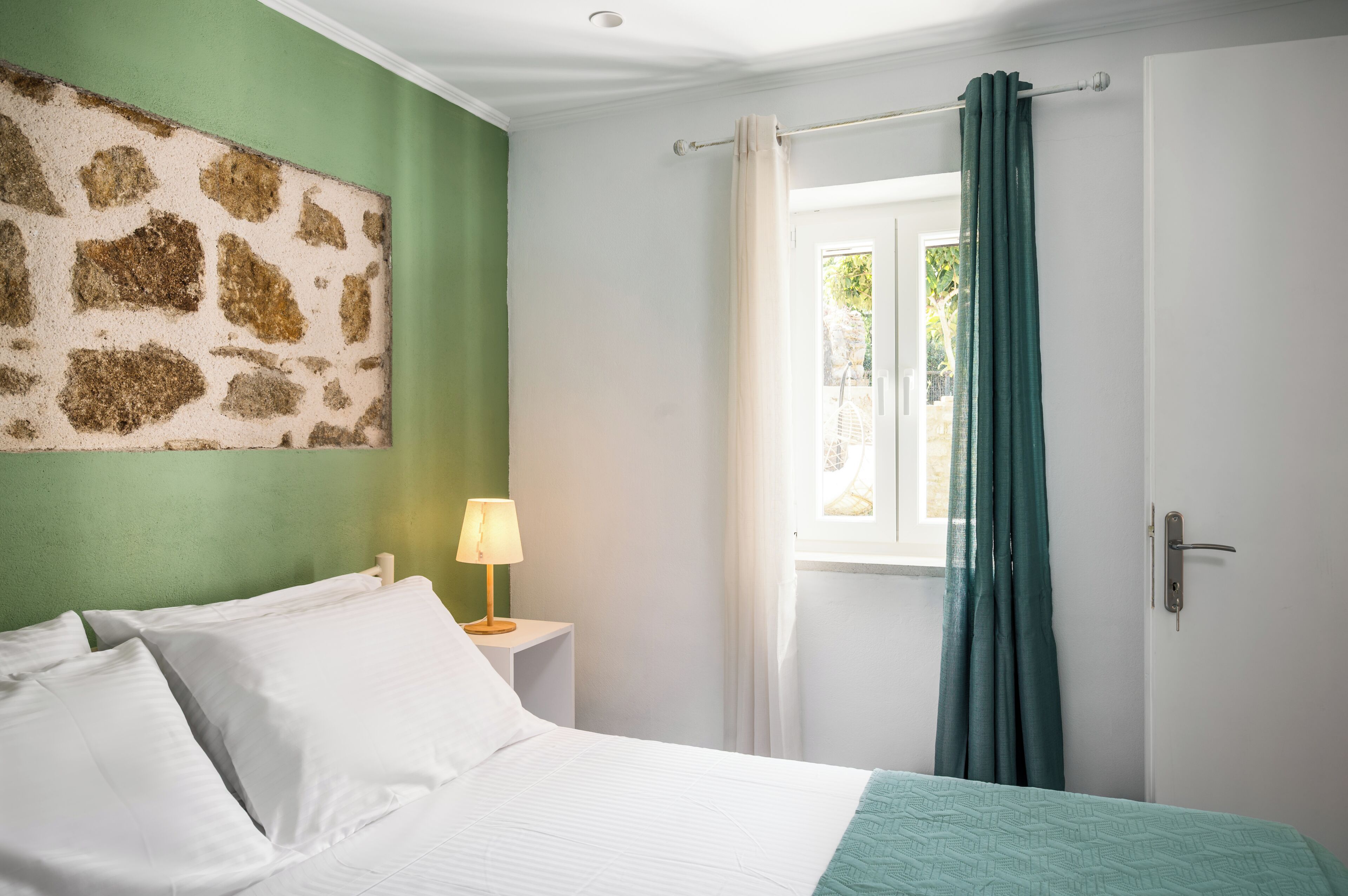 Une chambre à coucher avec un lit, une table de chevet avec une lampe, une fenêtre avec des rideaux et une porte.