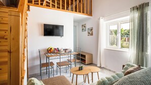 Ett rum i loftstil med en trätrappa, en matplats med stolar och ett bord, en tv som är monterad på väggen och ett fönster med gardiner.
