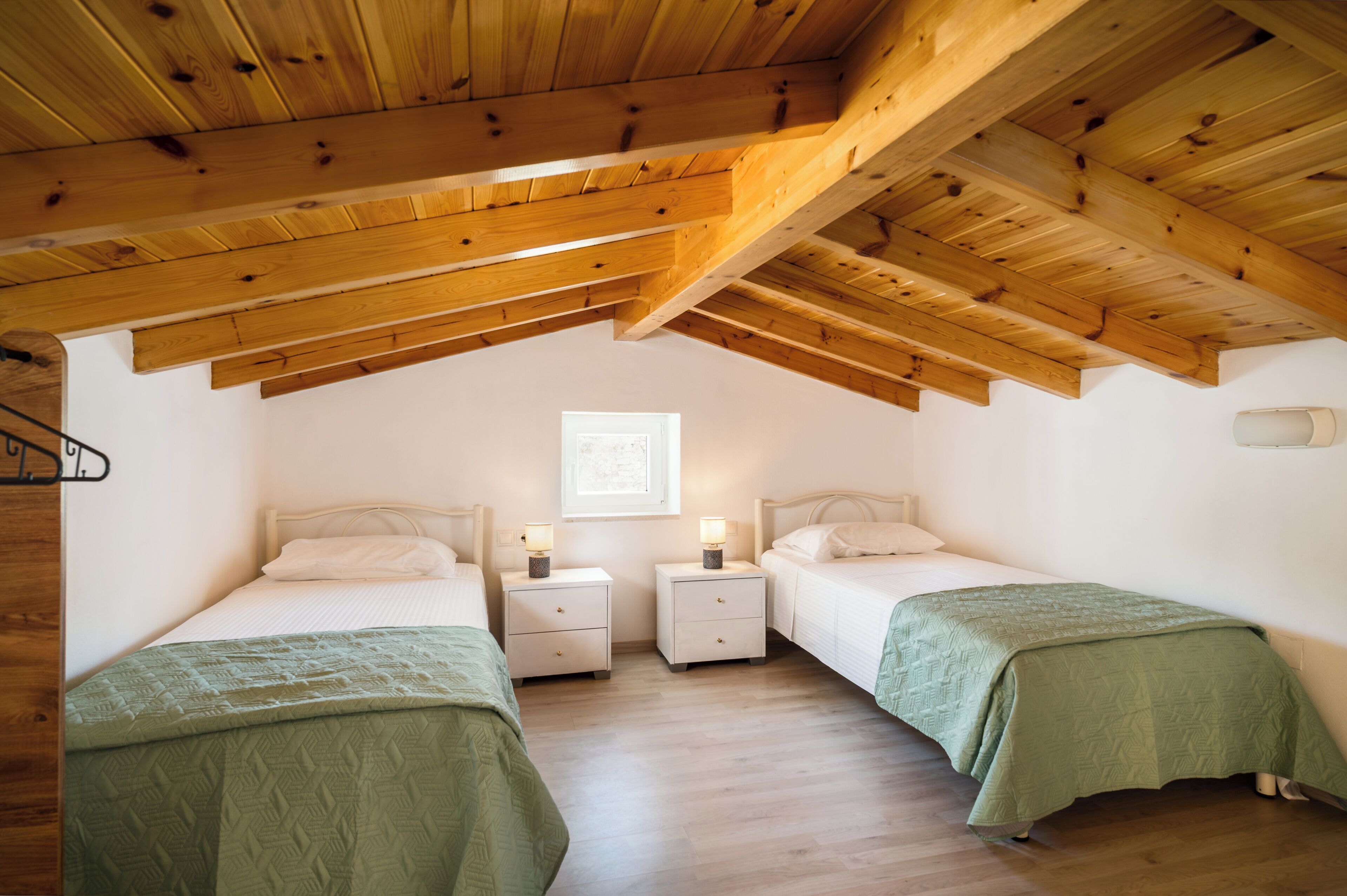 A bedroom with two beds, wooden ceiling beams, white walls, and a window.