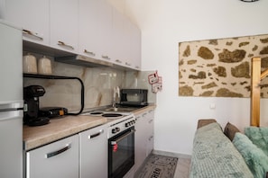 A compact kitchen with white cabinets, a Bosch coffee maker, a microwave, and a stove. - Alexandra's Stone House with Private Spa Tub by Konnect (Stroggili)