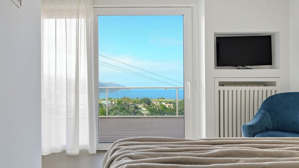 Ein Schlafzimmer mit einem Bett, einem blauen Sessel, einem Fernseher und Blick auf ein Gewässer.