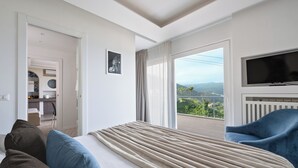 Ein Hotelzimmer mit Bett, Fernseher, Balkon und Aussicht sowie einem Sessel.