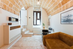 A cozy interior with a stone ceiling, a white console table, a brown sofa, a dining area with a small table and chairs, and a framed picture on the wall. - Volta Nova Collection – Historic Rooftop Retreat (Polignano a Mare)