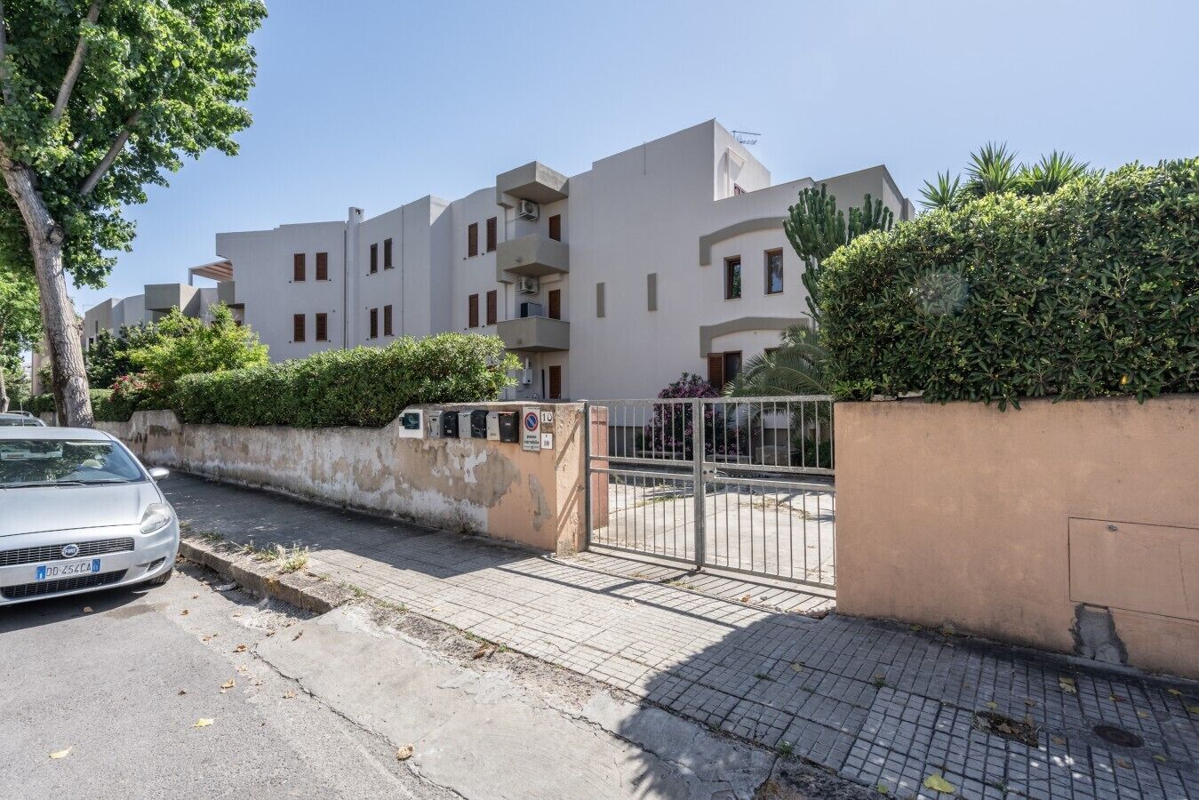 A residential building with a gated entrance, a parked car, and a paved driveway.