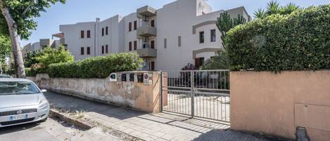 A residential building with a gated entrance, a parked car, and a paved driveway.