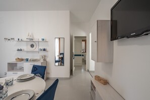 A modern kitchen with white cabinetry, a dining area with a round table and chairs, and a large mirror on the wall. - BlueLido House - Alghero (Alghero)
