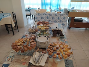 Un bufé con diversos postres y pasteles, un comedor con mesas y sillas, y una cama con colcha a rayas.