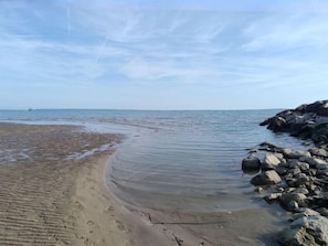 Una playa con arena, un promontorio rocoso y aguas tranquilas.